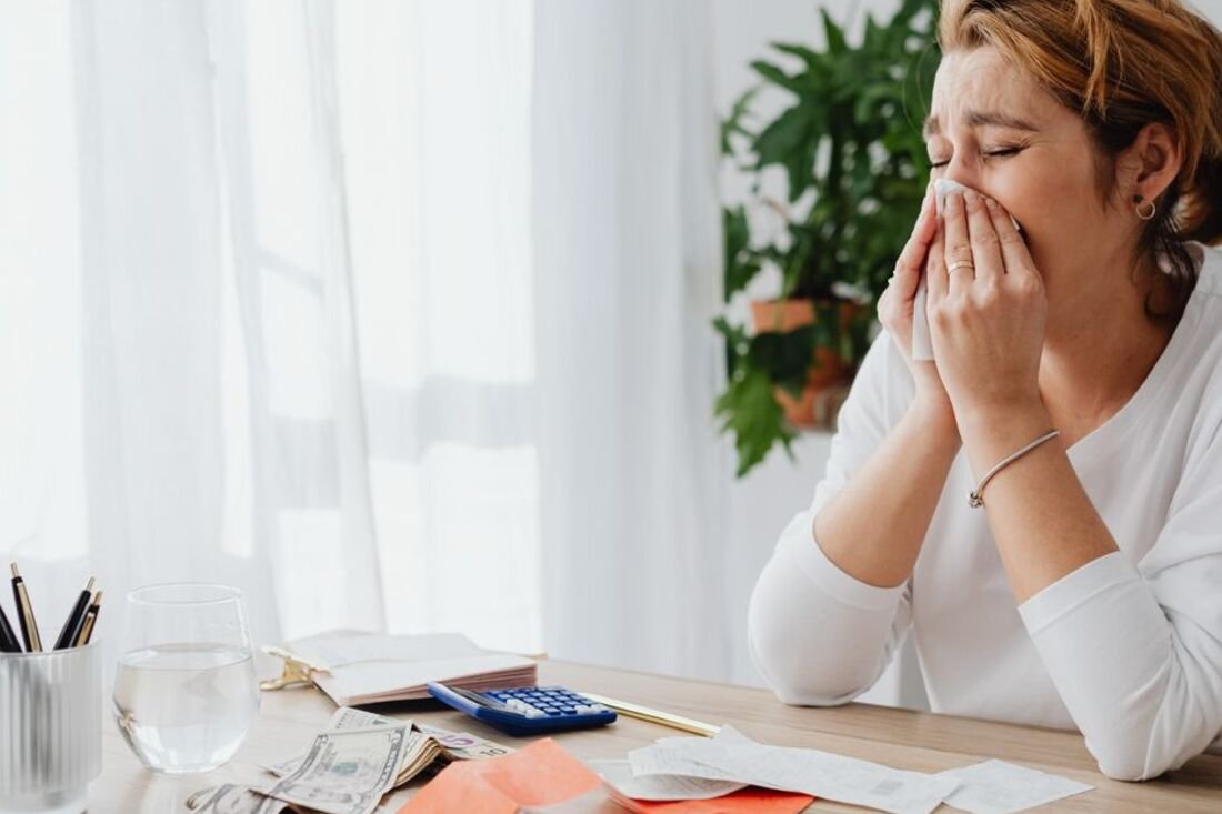 A woman at her kitchen table with statements and a calculator, hands over her mouth after reading the total.