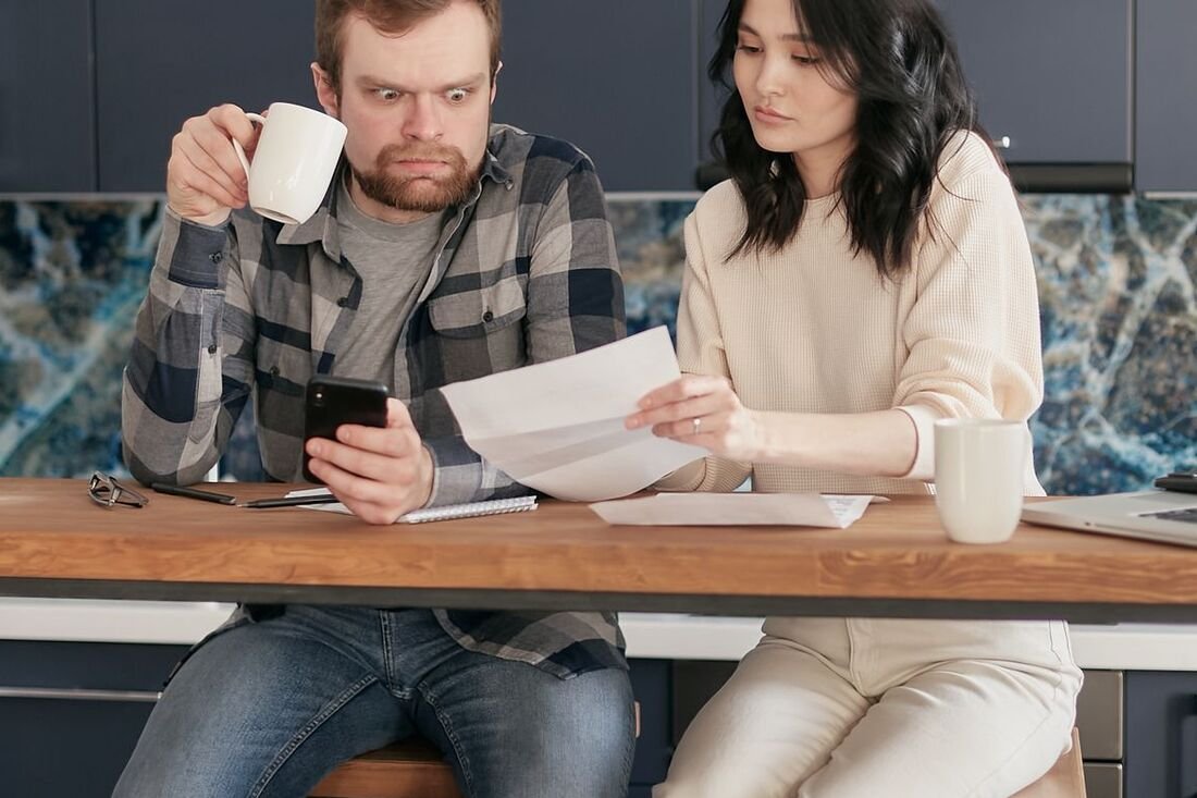 A couple at a kitchen counter going through medical statements together over coffee.